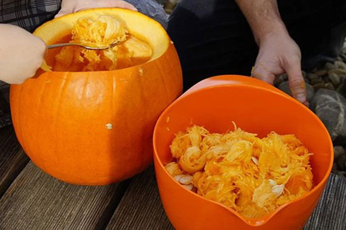 hand scooping pulp from pumpkin next to bucket of pumkin pulp