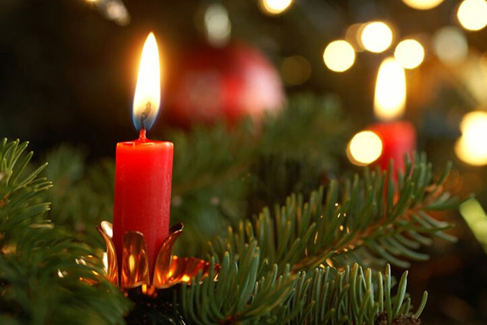 burning red candle amongst evergreen foliage