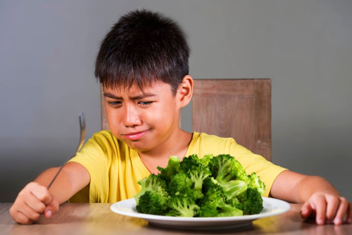 young boy scowling at plate of broccoli