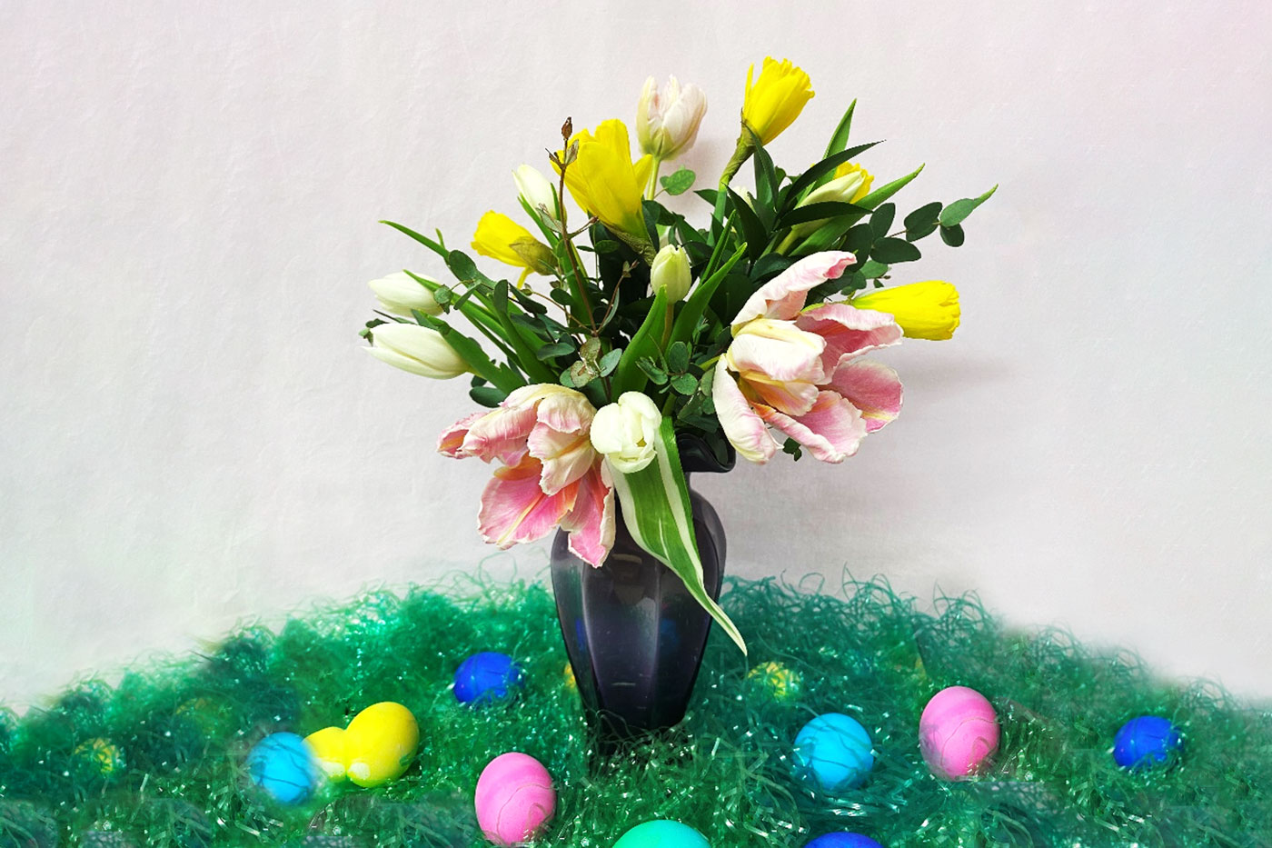 flowers in vase on table with green faux grass and colored eggs