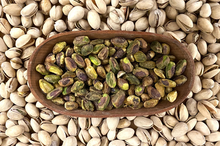 bed of light tan colored nuts with bowl of green nuts on top