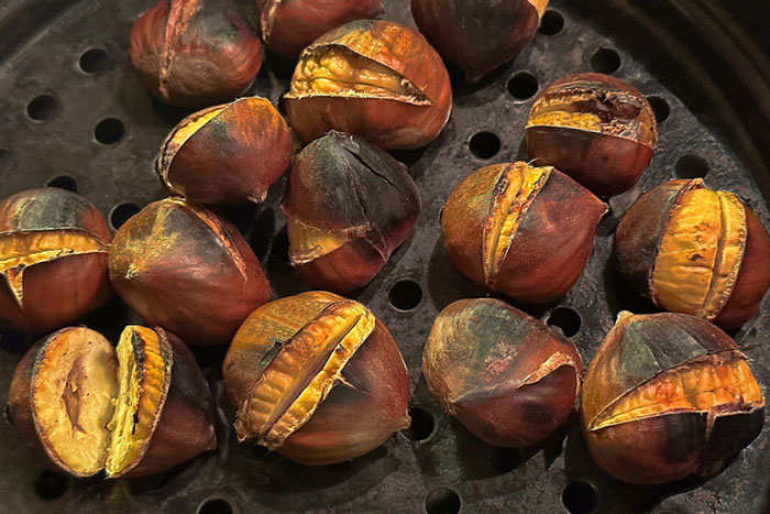 chared chestnuts with exposed flesh on metal grate 