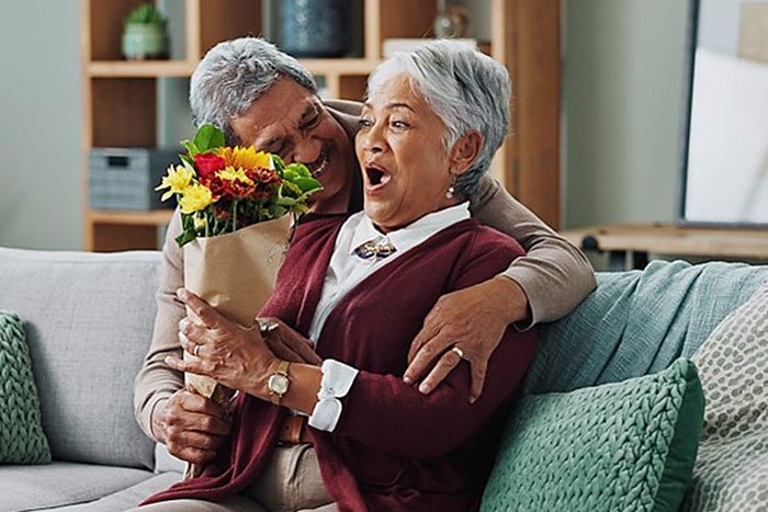 woman on couch recieving colorful bouquet of flowers from man behind